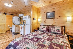 A wooden cabin interior with a bed, a kitchenette, and a wooden door. - Hudsons Hideaway Cabin on Creek in Beattyville! (Beattyville)