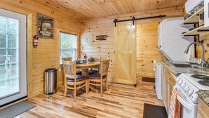 A wooden cabin interior with a dining area, kitchen, and a sliding door. - Hudsons Hideaway Cabin on Creek in Beattyville! (Beattyville)