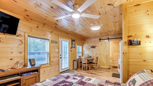 A wooden cabin room with a bed, a desk, a chair, a table, and a ceiling fan. - Hudsons Hideaway Cabin on Creek in Beattyville! (Beattyville)