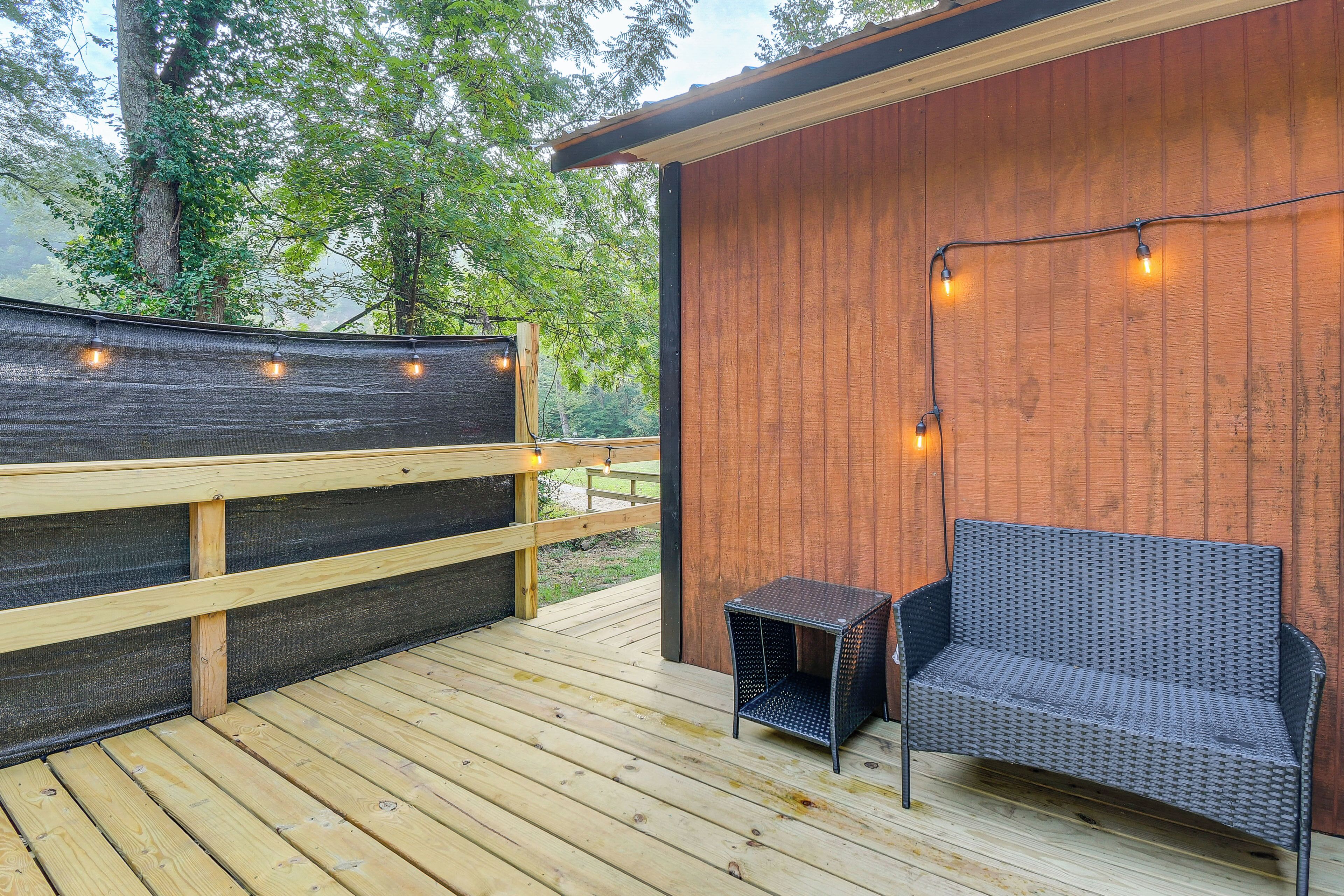 A wooden deck with a wicker sofa and a small table, surrounded by a wooden fence and string lights.