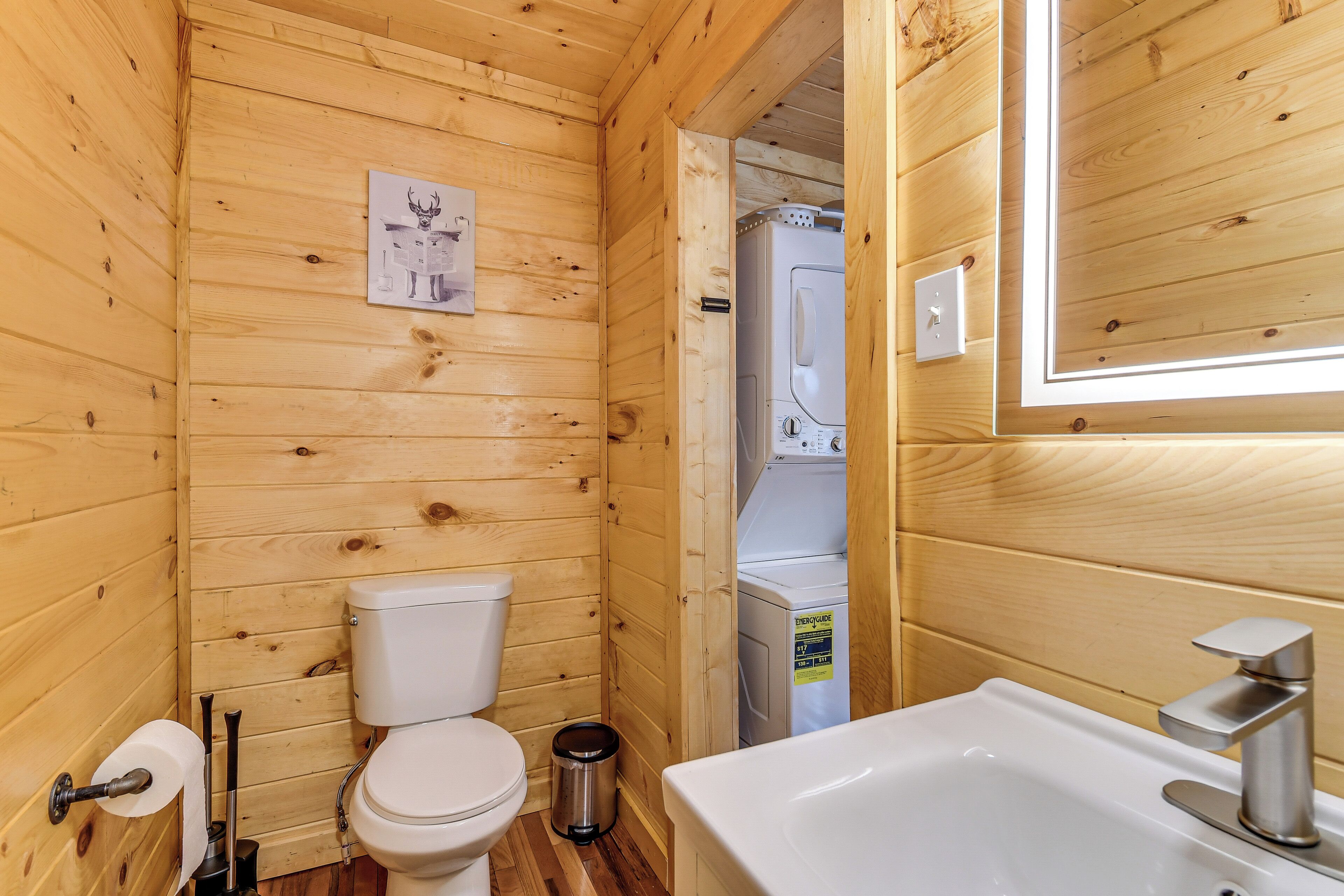 A wooden cabin bathroom with a toilet, sink, and a visible washing machine.