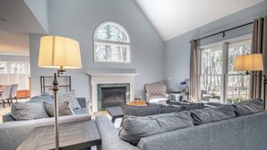 A modern living room with a fireplace, grey sofas, and a large window with curtains. - Secluded Haven, Minutes from UNC Chapel Hill and Carrboro (Chapel Hill)