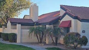 A two-story building with a red-tiled roof, beige exterior walls, and a red awning. There are palm trees and shrubs in front of the building. - NEW LOW RATE FOR THE SUMMER!                3-bed 2-bath townhome in Tempe (Tempe)