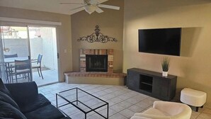 A living room with a fireplace, a ceiling fan, a flat-screen TV, and a sliding glass door leading to an outdoor patio. - NEW LOW RATE FOR THE SUMMER!                3-bed 2-bath townhome in Tempe (Tempe)