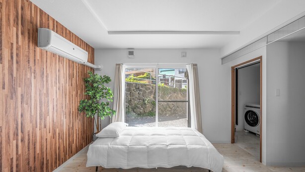 A bedroom with a bed, a potted plant, and a view of a stone wall and greenery outside. - OTARU SAMPO 2 (Otaru)