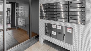 A modern interior with a glass door entrance, a wall-mounted mail slot system, and a control panel with emergency instructions. - OTARU SAMPO 2 (Otaru)