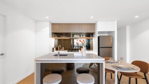 A compact kitchen with a central island, bar stools, a dining table with chairs, and a refrigerator.