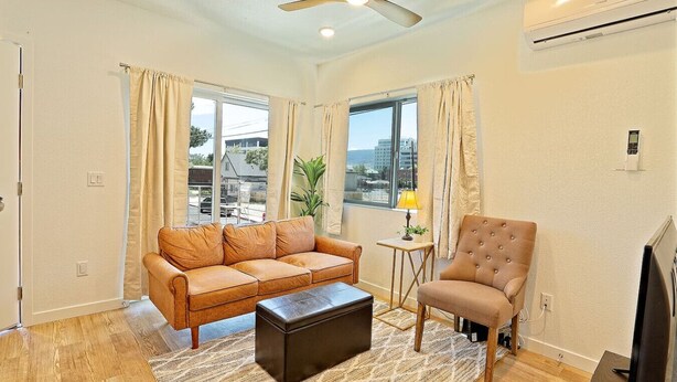 A living room with a sofa, armchair, and ottoman, a small table with a lamp, and a TV. - The Biggest Little Downtown Escape (Reno)