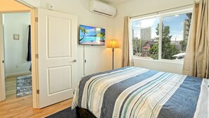 A bedroom with a bed, a TV on the wall, a window with curtains, and an air conditioning unit. - The Biggest Little Downtown Escape (Reno)