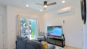 A modern living room with a grey sofa, a flat-screen TV, a ceiling fan, and a sliding glass door leading to an outdoor area. - Reno`s Downtown and Midtown Getaway (Reno)