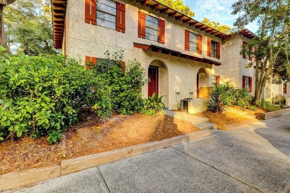 A two-story building with a stone facade, red shutters, and a central arched entrance.