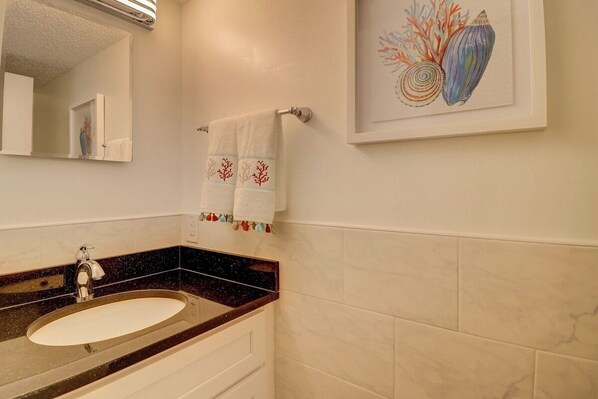 Une salle de bain avec un lavabo en marbre, un miroir et une œuvre d’art encadrée représentant des coquillages.