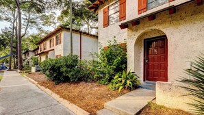 Una hilera de casas de estilo tradicional con puertas en arco y contraventanas rojas, un paseo pavimentado y un jardín bien cuidado.