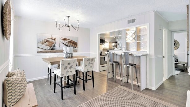 A modern kitchen with white cabinetry, a dining area with a wooden table and patterned chairs, and a bar area with stools. - Central Hilton Head Retreat 2BR Near Beaches (Hilton Head Island)