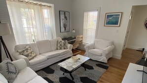 Ein modernes Wohnzimmer mit einem weißen Sofa, einem passenden Sessel, einem Couchtisch und einem Schreibtisch.