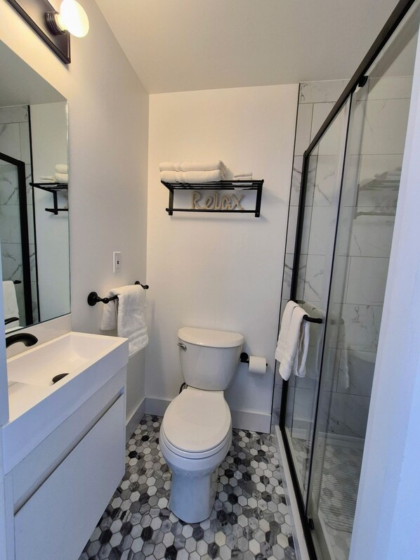 A modern bathroom with a white toilet, a sink, and a shower area. - Charming Home in Seaside (Bridgeport)