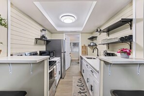 Moderni keittiö, jossa on valkoiset kaapit, keskellä oleva keittiösaareke ja sisäänrakennettu uuni.