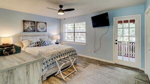 A bedroom with a bed, a ceiling fan, a TV mounted on the wall, and a door with a glass panel. - Hilton Head 2BR Escape w/ Pool & Sofa Bed (Hilton Head Island)