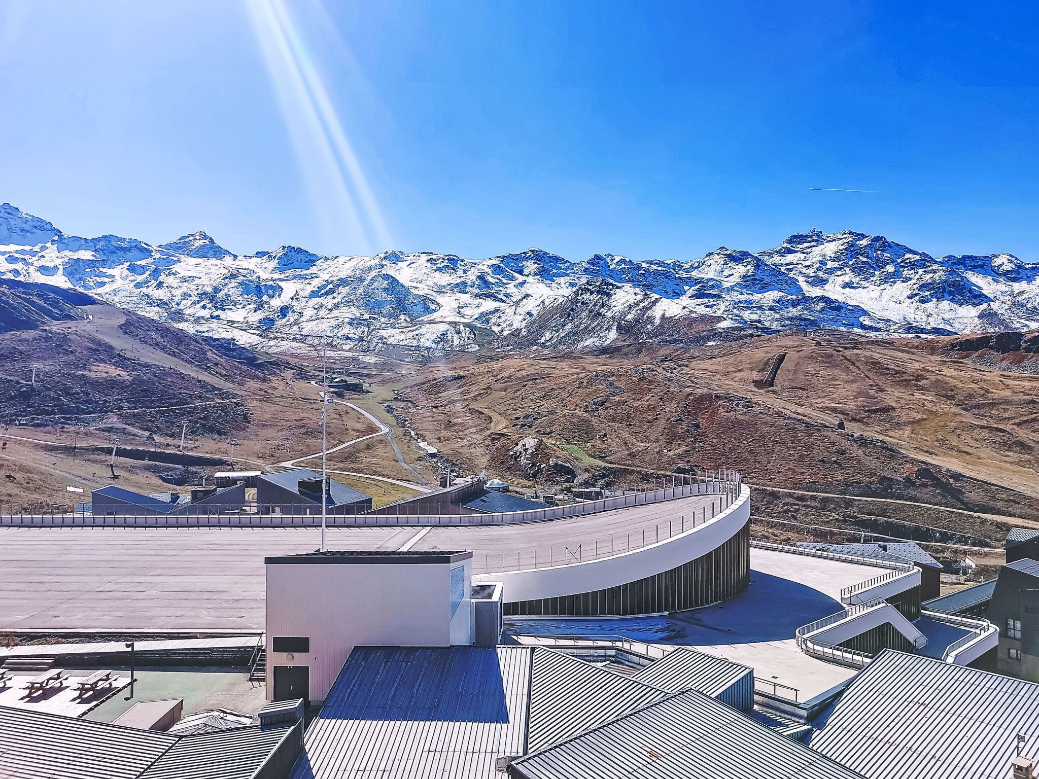 Ein modernes Gebäude mit gewölbter Dachform, umgeben von einer Berglandschaft mit schneebedeckten Gipfeln.