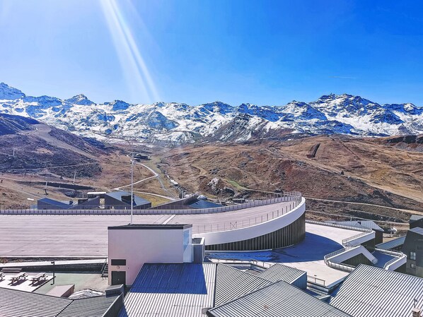 A modern building with a curved roof, surrounded by a mountainous landscape with snow-capped peaks.