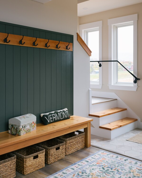 A modern interior with a wooden bench, wicker baskets, a wall-mounted coat rack, and a staircase.