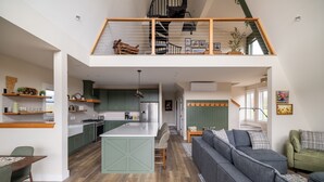 A spacious loft with a central kitchen, a dining area, and a living space with a staircase to an upper level. - Stowe A-Frame, Sauna, Hot Tub, Theater, Game Room, Arcade, Gym (Morristown)
