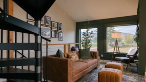 A modern living room with a brown leather sofa, a wooden bench, and a large window offering a view of the outdoors. - Stowe A-Frame, Sauna, Hot Tub, Theater, Game Room, Arcade, Gym (Morristown)