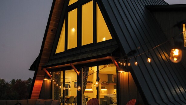 A modern house with a large glass window, a hot tub, and outdoor seating. - Stowe A-Frame, Sauna, Hot Tub, Theater, Game Room, Arcade, Gym (Morristown)