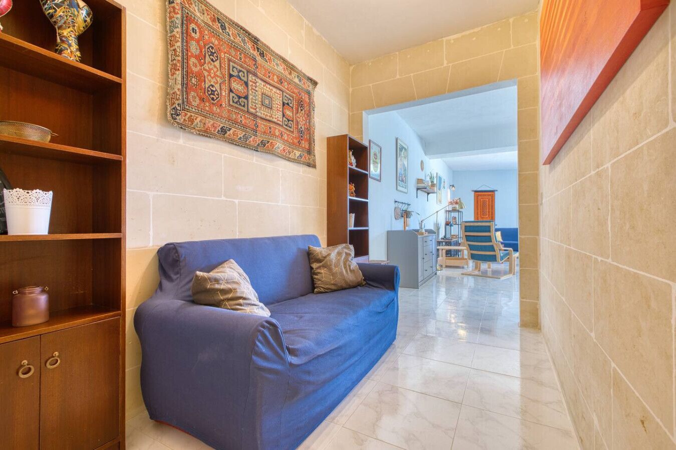 A hallway with a blue sofa, wooden shelves, and a patterned rug.