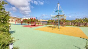 Ein Spielplatz mit Schaukeln, einer Kletterkonstruktion und einem umzäunten Bereich.