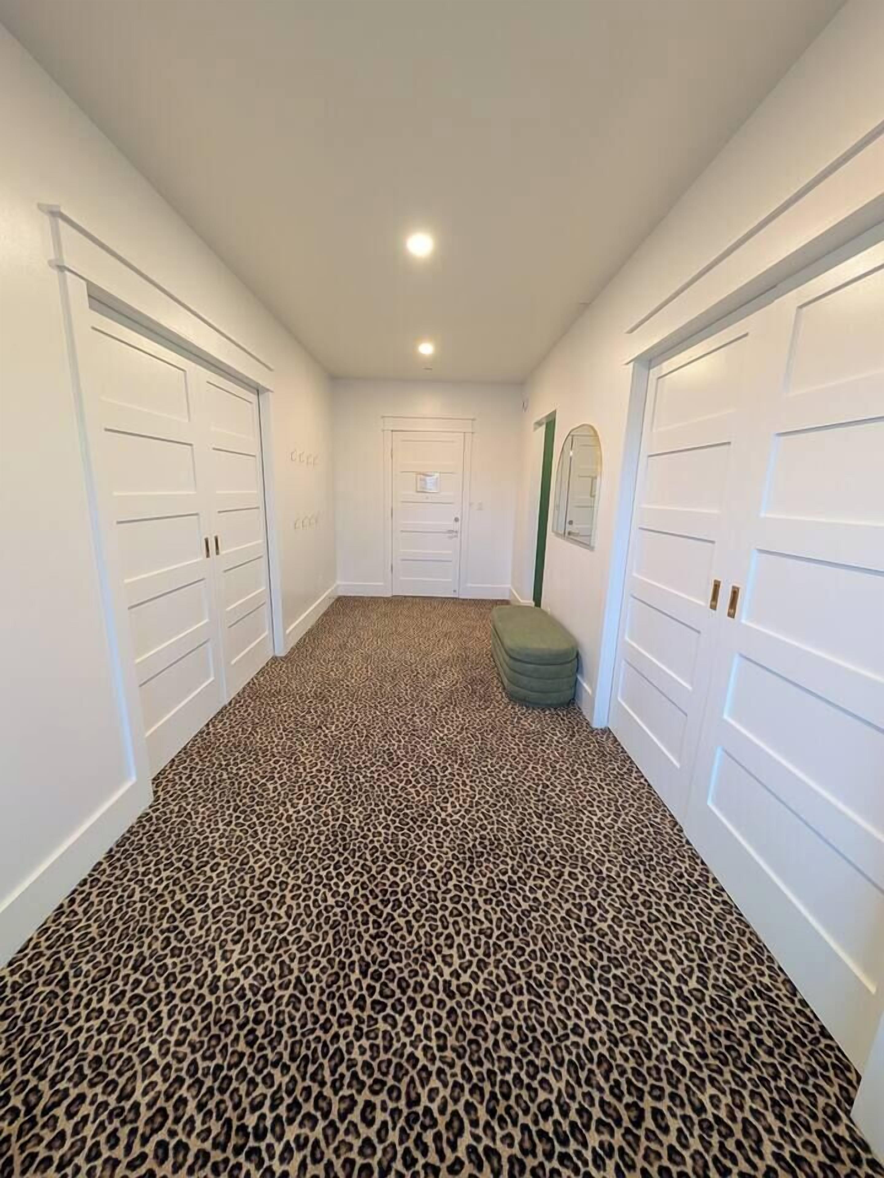 A hallway with white doors, a leopard print carpet, and a green ottoman.