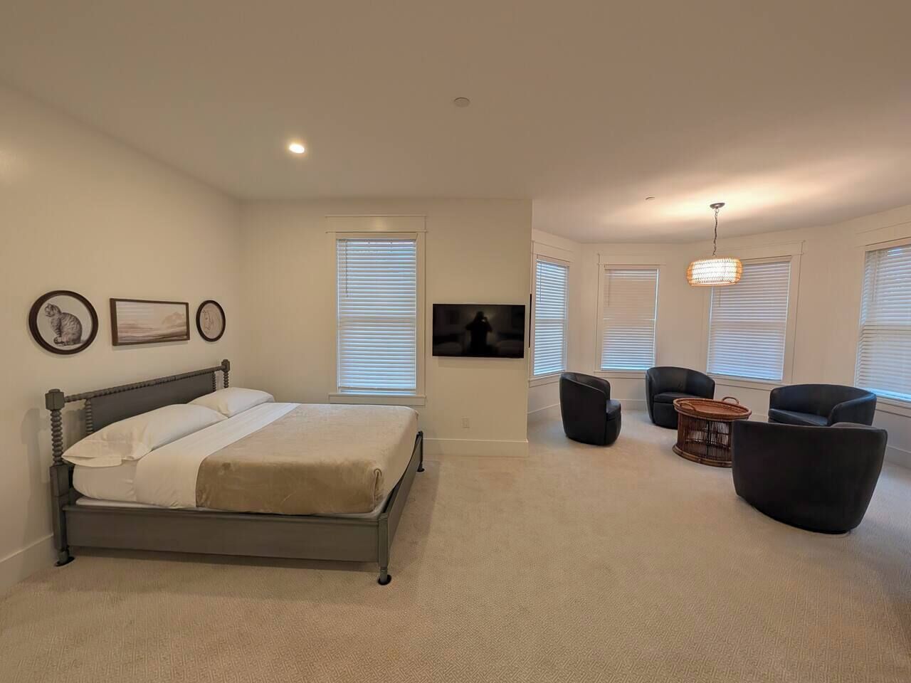 A spacious bedroom with a large bed, a TV mounted on the wall, and a seating area with chairs and a small table.
