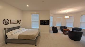 A spacious bedroom with a large bed, a TV mounted on the wall, and a seating area with chairs and a small table.