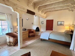 Une chambre à coucher avec un lit, une chaise, une commode, une cheminée et une fenêtre avec des rideaux.