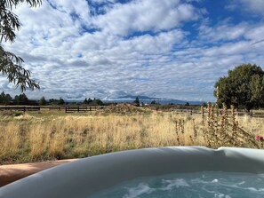 Un bain à remous installé dans un cadre naturel, avec vue sur les montagnes et un ciel nuageux.