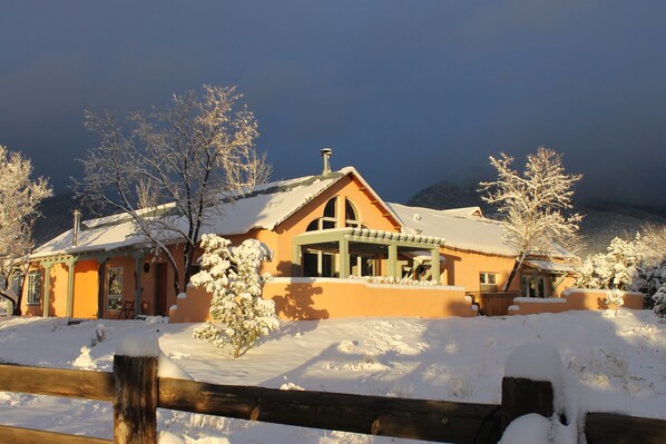 Une maison recouverte de neige, avec une clôture en bois devant.