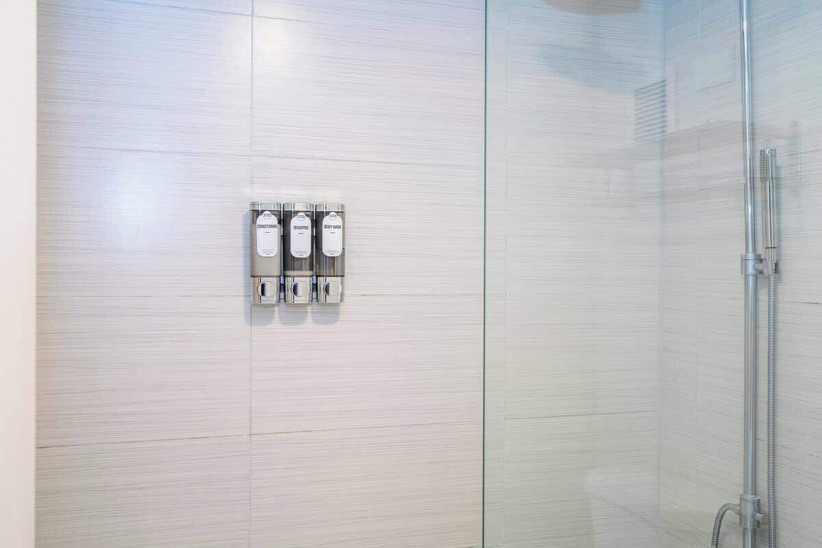 A bathroom with a glass shower enclosure, a wall-mounted soap dispenser, and a hand dryer.