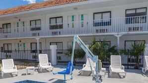 Ein Swimmingpool mit Liegestühlen, einem Rettungsschwimmerstand und einem Gebäude mit Balkonen.