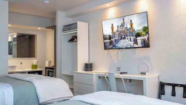 Ein Hotelzimmer mit einem Bett, einem Schreibtisch, einem Stuhl, einem an der Wand befestigten Fernseher und einem Kleiderschrank.
