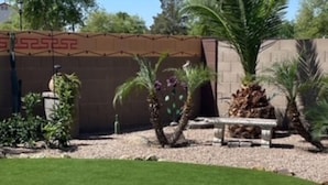 Un espace patio bien entretenu, agrémenté de gazon synthétique, d’un chemin en béton et de diverses plantes en pot.