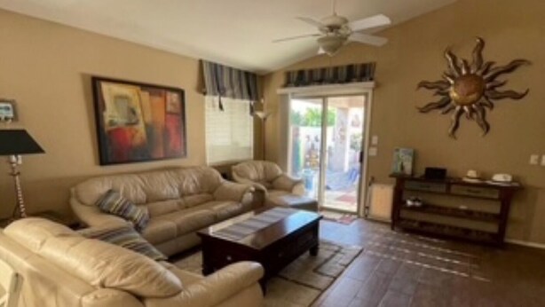 Un salon avec un ensemble de canapés beige, une table basse, un ventilateur de plafond et une décoration murale en forme de soleil.