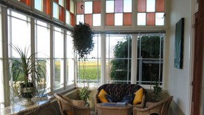 A sunlit room with wicker furniture, large windows, and a view of greenery outside.
