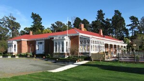 A two-story building with a red roof and large windows, surrounded by a well-maintained lawn and trees.