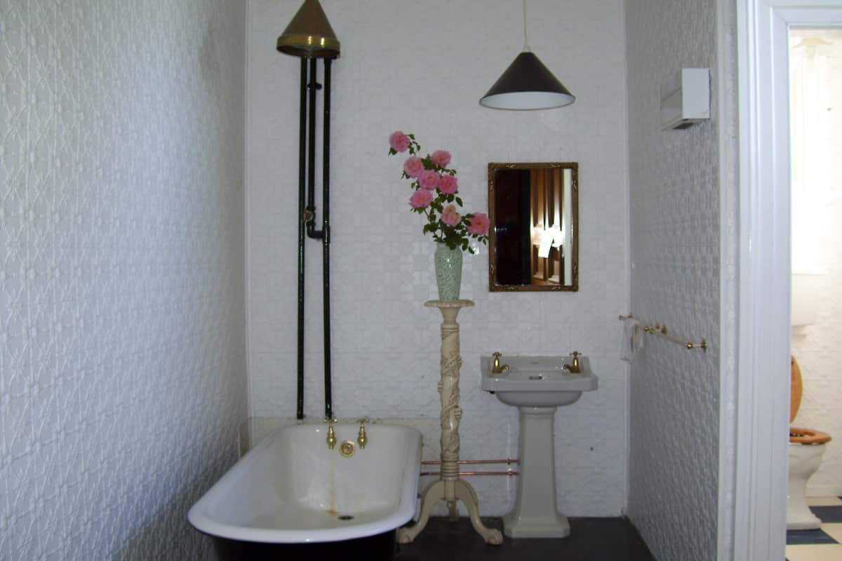 Casa de banho com banheira independente, lavatório suspenso, espelho e um vaso com flores.