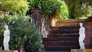 A garden with a brick staircase, two white statues, and various plants.