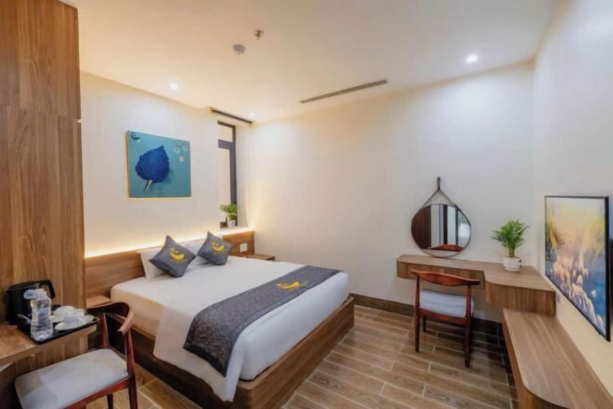 A modern hotel room with a large bed, a desk, a chair, a mirror, and artwork on the walls.
