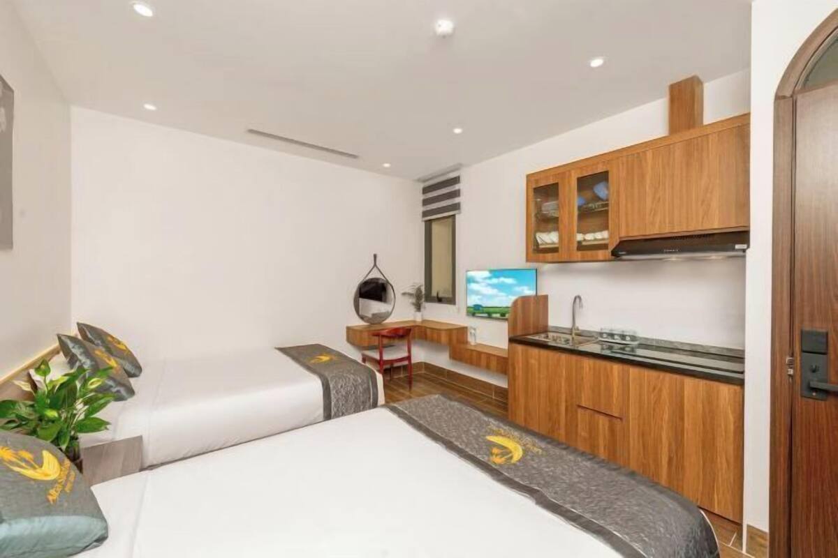 A compact hotel room with a bed, a small kitchenette, a TV, and a mirror.