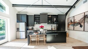 A modern kitchen with dark cabinetry, a central island, and a dining area with wicker chairs. - Luxury Getaway in East Texas, Pool • Jacuzzi (Bullard)