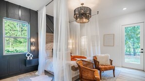 A bedroom with a large bed, a canopy, two wicker chairs, a chandelier, and a view of greenery outside. - Luxury Getaway in East Texas, Pool • Jacuzzi (Bullard)