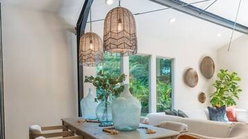 Un comedor con mesa de madera, sillas, lámparas colgantes y ventanas amplias que dan a vistas de vegetación exterior.
